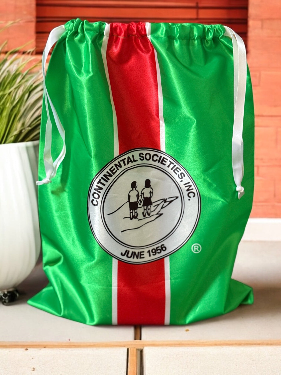 Green drawstring bag with red stripe and Continental Societies Inc. logo on a wooden surface.